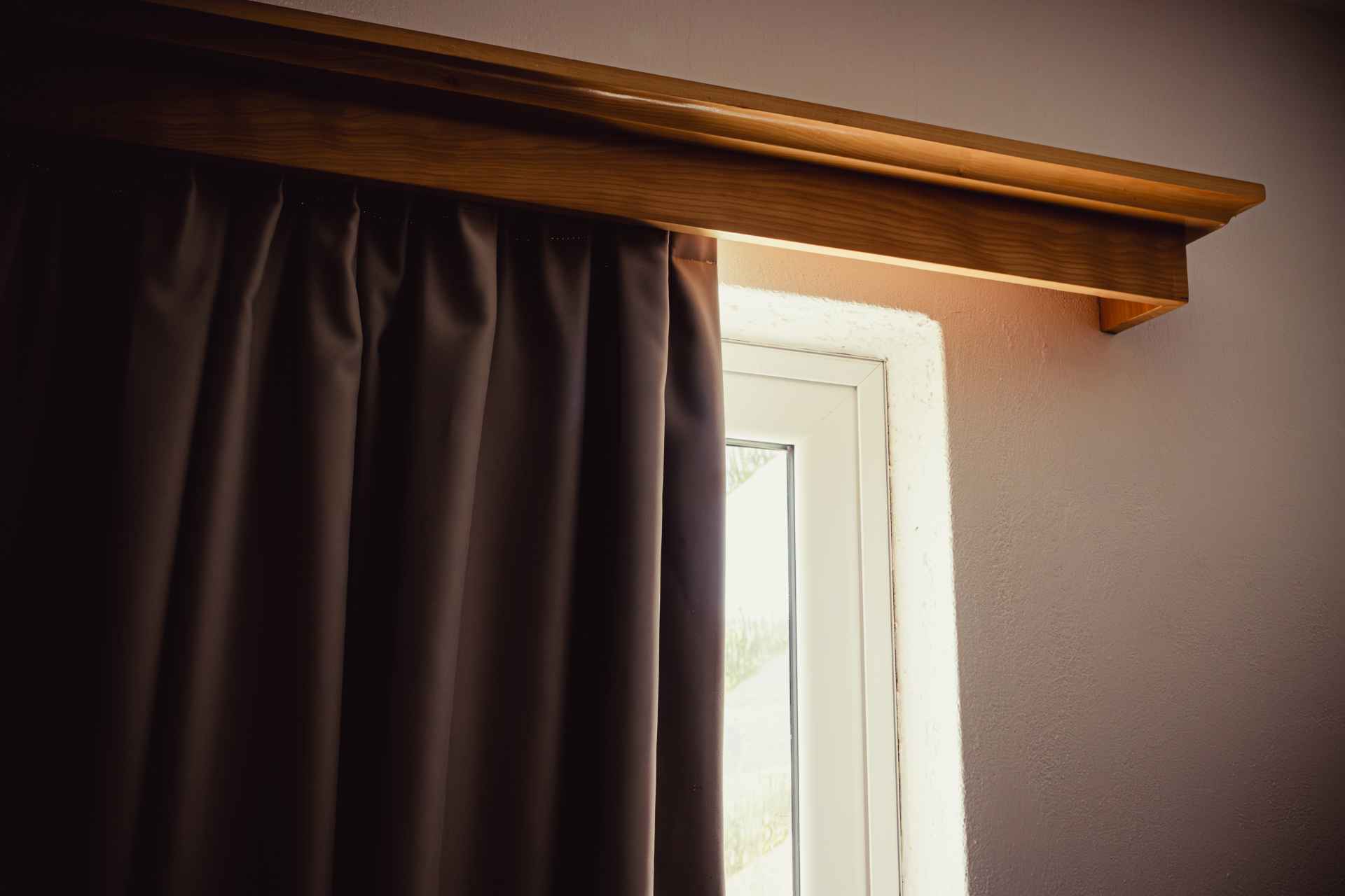 Window covered with dark brown thermal curtains slightly drawn to reveal a small peek of glass.