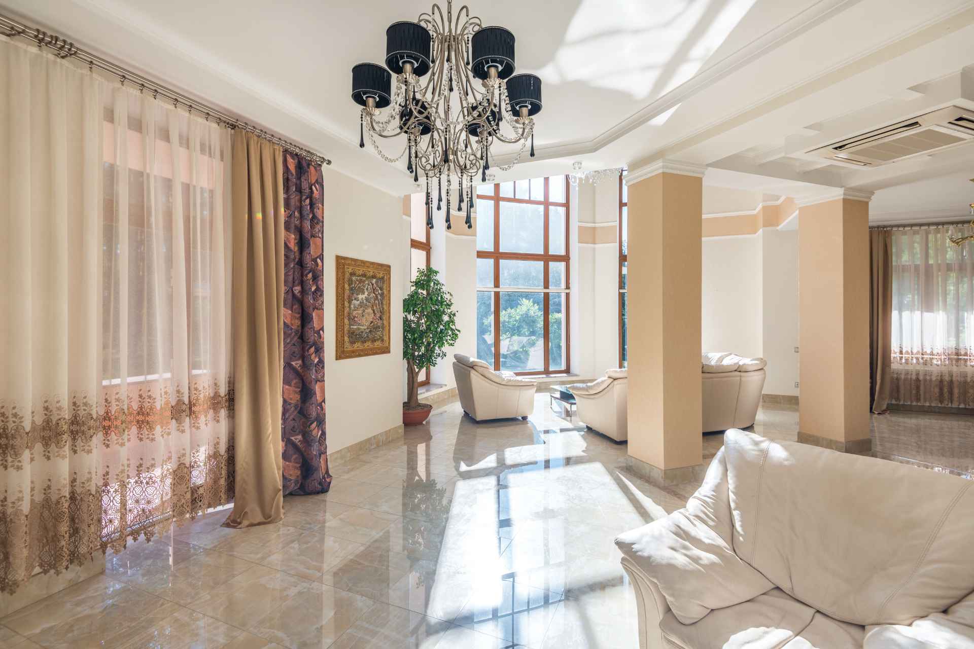 Spacious living room featuring elegant chandelier, large windows, and plush seating, expensive drapes and curtains, window coverings.